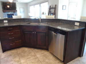 Kitchen featuring dark wood finish cabinetry, open floor plan, a stone fireplace, and stainless steel dishwasher