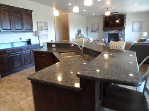 Kitchen featuring dark wood finish cabinetry, ceiling fan, a fireplace, open floor plan, and a kitchen breakfast bar