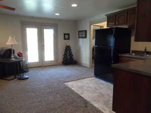 Basement kitchenette featuring dark countertops, french doors, light carpet, freestanding refrigerator, and recessed lighting