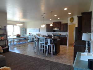 Kitchen featuring dark wood finish cabinetry, stainless steel appliances, a breakfast bar area, a kitchen island with sink, and hanging lights