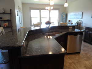 Kitchen with a breakfast bar, dishwasher, an island with sink, and dark stone countertops