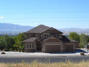 View of front of home featuring a mountain view, stone siding, an attached garage, concrete driveway, and asphalt shingles
