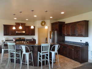 Kitchen featuring a kitchen breakfast bar, stainless steel appliances, dark stone counters, dark wood finish cabinetry, and decorative light fixtures