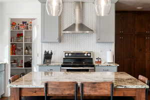 Kitchen featuring a kitchen breakfast bar, light stone counters, electric range, gray cabinets, and a kitchen island