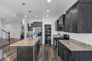 Kitchen featuring stainless steel appliances, light stone countertops, dark wood finished floors, dark wood finish cabinets, and pendant lighting