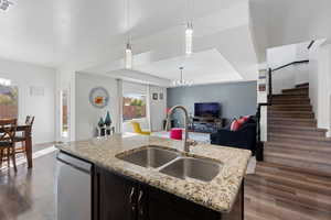 Kitchen featuring a tray ceiling, open floor plan, dishwasher, dark wood finished floors, and an island with sink