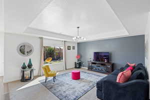 Carpeted living room featuring a tray ceiling, hanging lights, and a textured ceiling