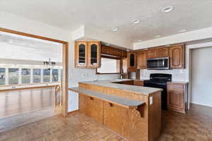 Kitchen featuring glass insert cabinets, black electric range oven, wood finish cabinetry, light countertops, and a kitchen breakfast bar