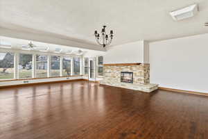 Unfurnished living room with dark wood-style flooring, a stone fireplace, a textured ceiling, a ceiling fan, and suspended lighting