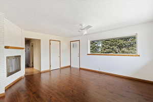 Unfurnished living room with a brick fireplace, dark wood-type flooring, ceiling fan, and a textured ceiling