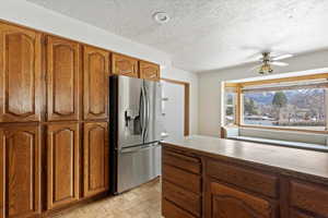 Kitchen featuring stainless steel fridge, a ceiling fan, wood finish cabinets, light countertops, and parquet flooring