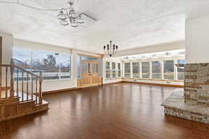 Unfurnished living room featuring a chandelier, a textured ceiling, and dark wood-style flooring