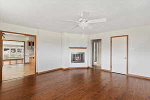 Unfurnished living room with ceiling fan, dark wood-style floors, a fireplace, and a textured ceiling