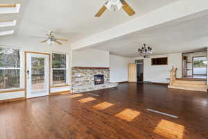 Unfurnished living room with dark wood finished floors, a ceiling fan, a stone fireplace, and a skylight