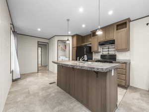 Kitchen featuring a breakfast bar area, black appliances, decorative light fixtures, crown molding, and an island with sink