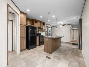 Kitchen with black appliances, dark countertops, a center island with sink, hanging light fixtures, and wood finish cabinetry