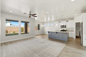 Kitchen featuring light stone counters, light wood finished floors, pendant lighting, ceiling fan, and open floor plan