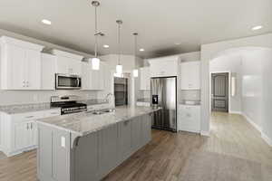 Kitchen featuring stainless steel appliances, wood tiled floors, light stone counters, a center island with sink, and white cabinets