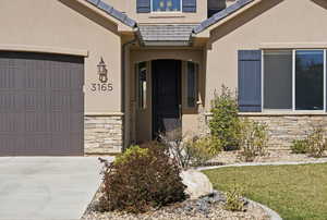 Doorway to property featuring stone siding, a garage, stucco siding, and driveway