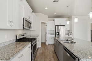 Dual tone kitchen featuring stainless steel appliances, light stone countertops, wood tiled floors, hanging light fixtures, and an island with sink