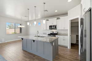 Dual tone kitchen with stainless steel appliances, wood tiled floors, light stone counters, an island with sink, and dual tone cabinets