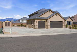 View of front of house with stucco siding, an attached garage, stone siding, and driveway