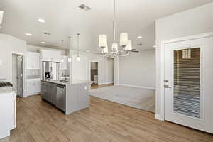 Kitchen with light stone countertops, light wood-style flooring, suspended lighting, stainless steel appliances, and two tone cabinets