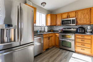 Kitchen with stainless steel appliances, lofted ceiling, wood finish cabinets, dark wood-style flooring, and decorative backsplash
