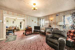 Carpeted living area with suspended lighting, a textured ceiling, and wallpapered walls