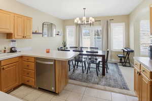Kitchen featuring light countertops, a peninsula, dishwasher, hanging lights, and light tile patterned flooring