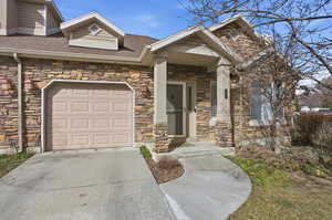 View of front of house with stone siding, concrete driveway, roof with shingles, and a garage