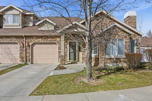 View of front facade with stone siding, driveway, a shingled roof, and a front yard