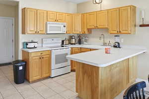 Kitchen featuring white appliances, a peninsula, light wood finish cabinets, and light countertops