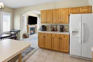 Kitchen featuring white refrigerator with ice dispenser, light countertops, a fireplace, light carpet, and light tile patterned floors