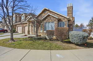 View of front of home with driveway, stone siding, and a chimney