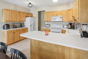 Kitchen featuring white appliances, light countertops, light tile patterned floors, light wood finish cabinets, and a peninsula