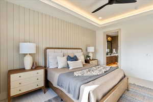 Carpeted bedroom with ensuite bathroom, a ceiling fan, and a tray ceiling