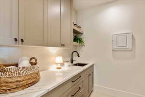 Bar featuring light stone countertops, open shelves, decorative backsplash, and gray cabinetry