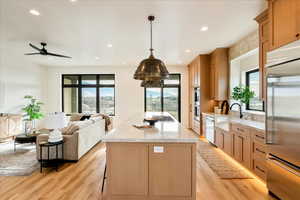 Kitchen featuring stainless steel appliances, open floor plan, light stone counters, a kitchen island, and light wood finished floors