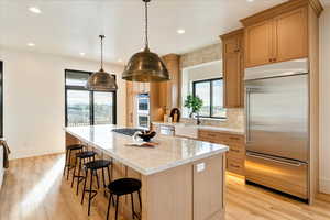Kitchen with stainless steel appliances, tasteful backsplash, a kitchen bar, light wood-style flooring, and light stone counters