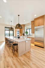 Kitchen with light wood finish cabinets, a spacious island, a kitchen bar, stainless steel appliances, and decorative backsplash