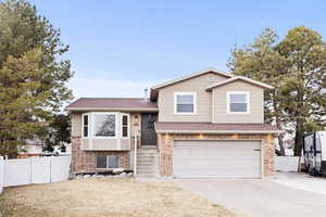 Tri-level home featuring brick siding, an attached garage, driveway, and a shingled roof