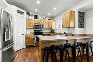 Kitchen featuring stainless steel appliances, a peninsula, a breakfast bar, light countertops, and vaulted ceiling