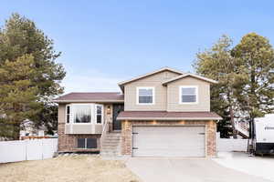 Split level home featuring concrete driveway, brick siding, a garage, and a shingled roof