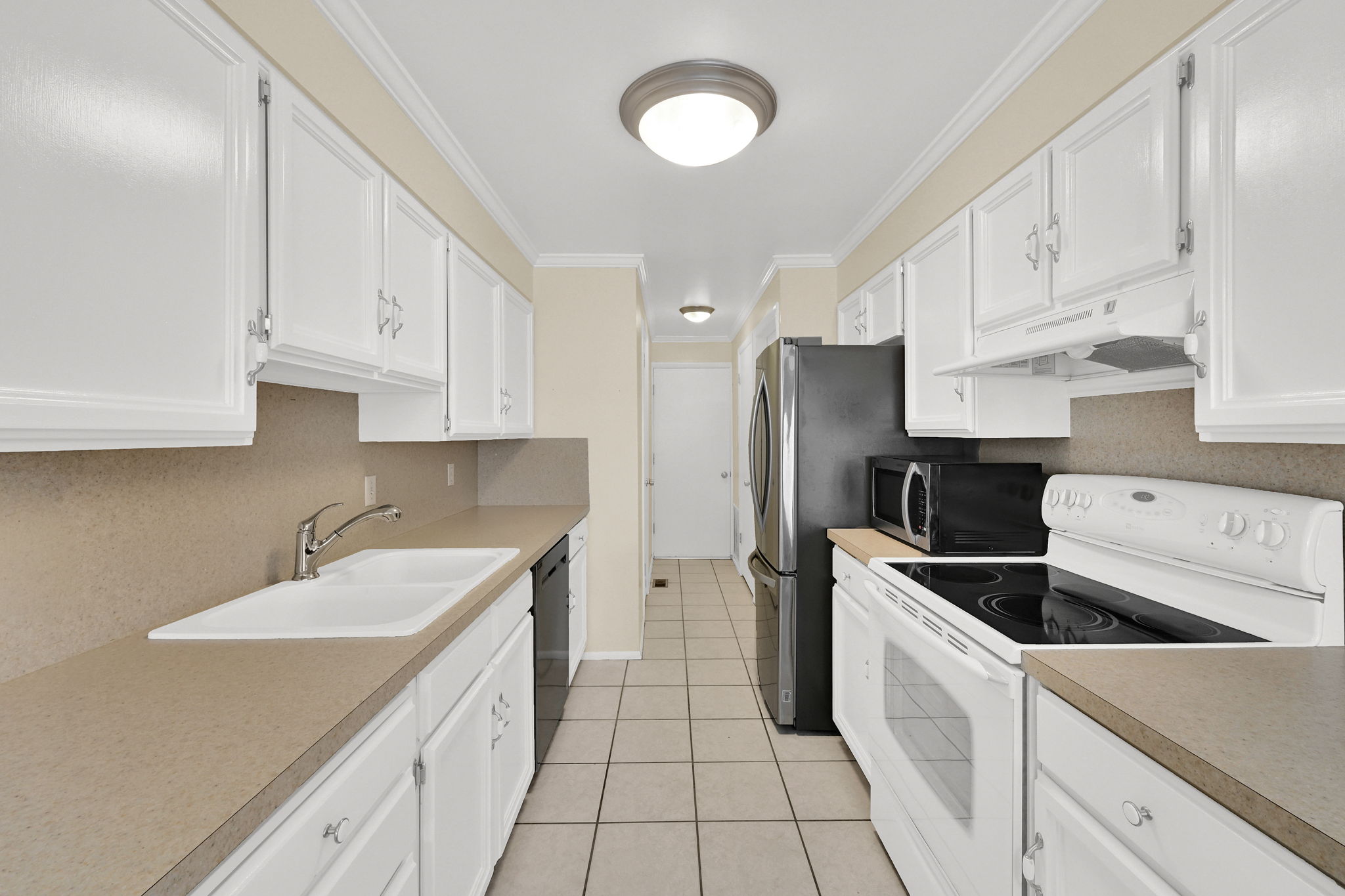 Kitchen with stainless steel appliances, white cabinetry, ornamental molding, light countertops, and light tile patterned floors