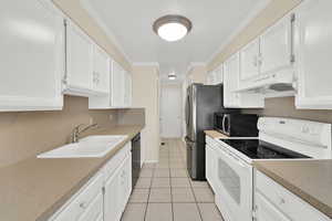 Kitchen with stainless steel appliances, white cabinetry, ornamental molding, light countertops, and light tile patterned floors