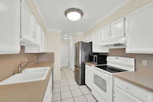 Kitchen with white range with electric stovetop, white cabinetry, ornamental molding, stainless steel microwave, and light countertops