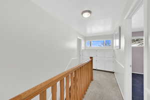 Hallway featuring an upstairs landing and light carpet