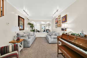 Living room with ornamental molding, arched walkways, track lighting, and light colored carpet