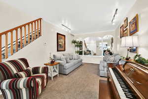 Living area with arched walkways, track lighting, ornamental molding, and light colored carpet